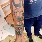 Фото татуировки с изображением Эдди, талисмана группы Iron Maiden, на руке. Реалистичный рисунок в черно-серых тонах, передающий агрессивный образ персонажа.