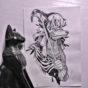 Фото тату Анубиса с косой в стиле old school. Яркий рисунок с четкими контурами и насыщенными цветами, изображающий древнеегипетского бога с атрибутами жнеца.