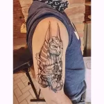 Фото тату на руке: изображение бога Анубиса, выполненное в стиле blackwork с использованием плотных черных линий и эффекта дымки.