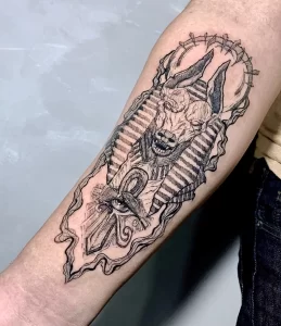 Фото тату Анубиса на предплечье в стиле Blackwork. Использование только черного цвета, сложные узоры и геометрические формы.