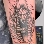 Фото тату Анубиса на предплечье с эффектом вырывающейся кожи. Динамичный и реалистичный рисунок.