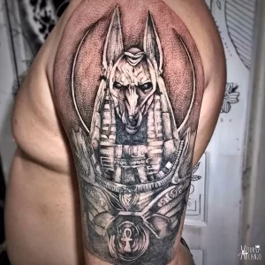 Фотография черно-серой татуировки Анубиса на плече, выполненной в технике dotwork. Детализированный рисунок с использованием точек.
