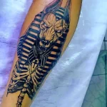 Фото татуировки на руке в стиле Blackwork с изображением головы Анубиса и скелета. Контрастный рисунок с использованием только черного цвета.