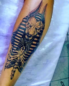 Фото татуировки на руке в стиле Blackwork с изображением головы Анубиса и скелета. Контрастный рисунок с использованием только черного цвета.