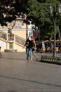 Фото тату на предплечье мужчины, идущего с женщиной по улице. Татуировка выполнена в черных тонах, изображает абстрактный узор.