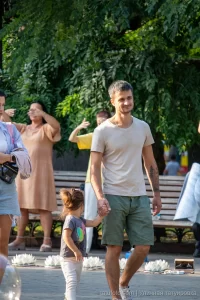Фото тату на руке мужчины, держащего за руку маленькую девочку. Татуировка изображает темные деревья на фоне светлой кожи.