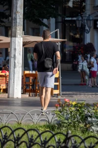 Фото тату на руке мужчины, идущего по улице. Видна часть татуировки в темных тонах, с растительными элементами.