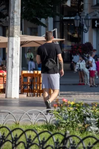 Фото тату на руке мужчины, идущего по улице. Видна часть татуировки в темных тонах, с растительными элементами.