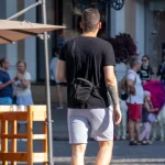 Фото тату на руке мужчины, идущего по улице. Видна часть татуировки в темных тонах, с растительными элементами.