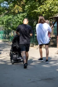 Фото татуировки на спине мужчины: темный, абстрактный рисунок, на фоне которого видна детская коляска и женщина с ребенком.