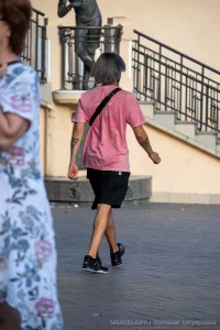 Фотография татуировки в виде черного треугольника на руке мужчины, стоящего на улице. Мужчина одет в розовую футболку.
