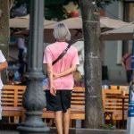 Фото минималистичной татуировки в виде черного треугольника на руке мужчины. Мужчина стоит спиной к камере в городской среде.