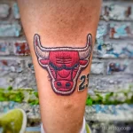 Фото тату на ноге с изображением головы быка, логотипа Chicago Bulls и номера 23, выполненное в ярких красных и синих тонах.
