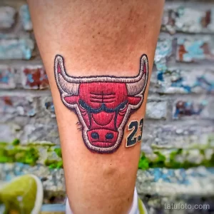 Фото тату на ноге с изображением головы быка, логотипа Chicago Bulls и номера 23, выполненное в ярких красных и синих тонах.