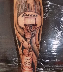 Фото тату на руке: детализированный портрет Майкла Джордана с логотипом Lakers и видом на город. Выполнено в черно-серых тонах.