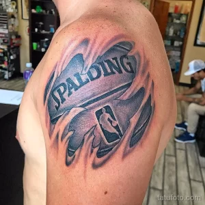 Фото тату на плече, изображающее логотип Spalding и NBA на фоне красных языков пламени. Татуировка выполнена в ярких и контрастных цветах.