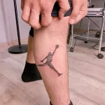 Фото тату силуэта Майкла Джордана в прыжке, выполненного в черном цвете на ноге.