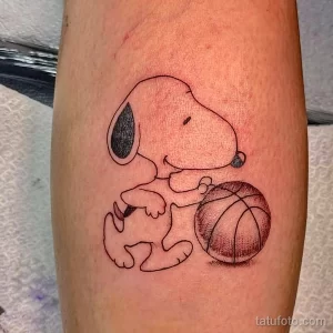 Черно-белая татуировка на руке, изображающая Снупи из Peanuts, обнимающего баскетбольный мяч.
