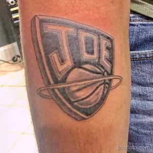 Фото тату на предплечье с изображением баскетбольного щита и надписью 'JOE'. Черно-белая гамма, минималистичный стиль.