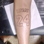 Фото минималистичной татуировки с надписью "BRYANT" и номером "24" на руке. Черно-белый рисунок, четкие линии.