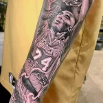 Фото тату портрета Коби Брайанта в форме Lakers на предплечье, с элементами розы и брызгами краски. Реалистичный рисунок татуировки.