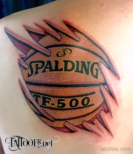 Фото тату баскетбольного мяча, словно удерживаемого руками, с логотипом Spalding. Детализированный рисунок татуировки на плече.