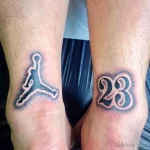 Фото двух минималистичных татуировок на лодыжках: логотип Jumpman и номер 23. Черно-белый рисунок, простой стиль.