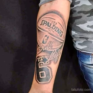 Фото тату на предплечье с изображением баскетбольного мяча Spalding и номера 5. Реалистичный дизайн с надписью 'Ball is Life'.