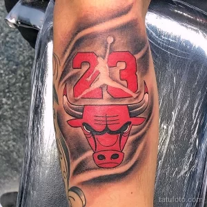 Фото татуировки с изображением головы быка (логотип Chicago Bulls) и номера 23, выполненной в красных и черных тонах на предплечье. Татуировка для поклонников баскетбола.