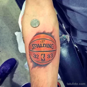 Фото тату на предплечье: реалистичное изображение баскетбольного мяча Spalding с номерами 32 и 33.