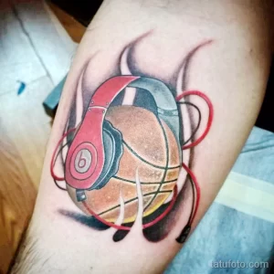 Фото тату на руке: яркий рисунок баскетбольного мяча с красными наушниками Beats, дополненный красными брызгами и линиями.