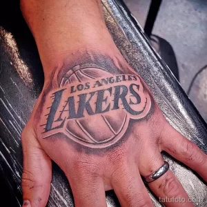 Фото тату логотипа баскетбольной команды Los Angeles Lakers на руке. Черно-серый рисунок татуировки с детальной проработкой элементов.