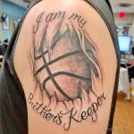 Фото тату с надписью 'I am my brother's keeper' и изображением двух переплетенных рук на фоне крыльев. Черно-серый рисунок на плече.