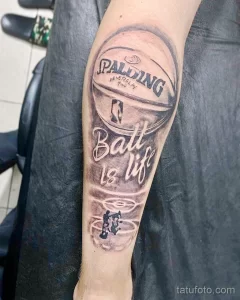 Фото тату баскетбольного мяча Spalding на предплечье. Черно-серый рисунок с надписью 'Ball is life' и силуэтом игрока.
