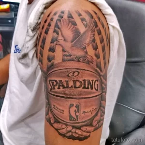 Фото тату с изображением баскетбольного мяча Spalding и орла, выполненное в черно-серых тонах на плече, с использованием эффекта брызг.