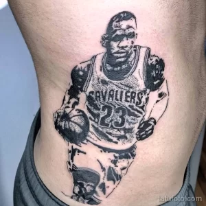 Фото тату с изображением Леброна Джеймса в форме Cavaliers, в динамичной позе с баскетбольным мячом, выполненное в черно-белых тонах на боку.