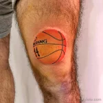 Фото тату реалистичного баскетбольного мяча Spalding с номером 14 на колене. Яркий оранжевый цвет и четкие линии.