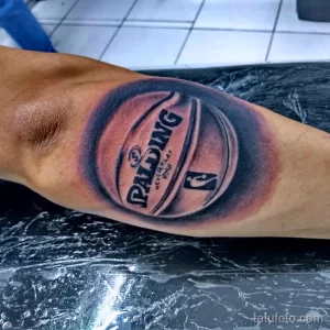 Фото реалистичной татуировки на руке с изображением баскетбольного мяча Spalding. Тату выполнено в черно-серых тонах с яркими бликами.