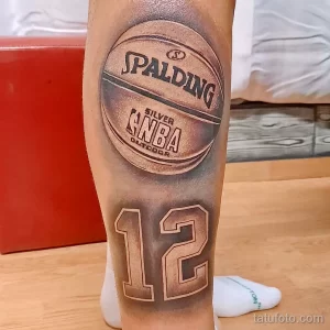 Фото тату на ноге: реалистичное изображение баскетбольного мяча Spalding с логотипом и надписью 'SILVER NBA OUTDOOR'. Черно-серые тона, детализированная проработка текстуры мяча.