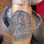 Фото татуировки баскетбольного мяча с надписью "True to the Game" на предплечье. Черно-белый рисунок татуировки в стиле графика.