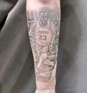 Фото тату с изображением Леброна Джеймса в форме Los Angeles Lakers на предплечье, выполненное в реалистичном стиле с использованием черно-серых оттенков.
