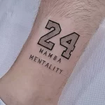 Фото татуировки на запястье с изображением номера 24 и надписи "Mamba Mentality". Стиль графика, черно-белое изображение, минималистичный дизайн.