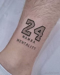 Фото татуировки на запястье с изображением номера 24 и надписи "Mamba Mentality". Стиль графика, черно-белое изображение, минималистичный дизайн.