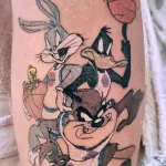Фото татуировки на предплечье с изображением персонажей Looney Tunes (Bugs Bunny, Daffy Duck, Taz, Tweety) и баскетбольного мяча. Яркие цвета, мультяшный стиль.