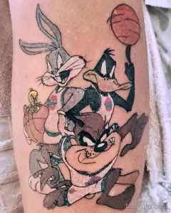 Фото татуировки на предплечье с изображением персонажей Looney Tunes (Bugs Bunny, Daffy Duck, Taz, Tweety) и баскетбольного мяча. Яркие цвета, мультяшный стиль.