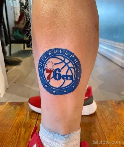 Фото тату красочного логотипа баскетбольной команды Philadelphia 76ers с баскетбольным мячом и звездами, выполненное на икре.