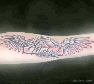 Фото татуировки на плече с изображением ангельских крыльев и надписи 'Michael' в рамке.