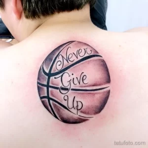 Фото татуировки баскетбольного мяча с надписью 'Never Give Up' на спине. Рисунок выполнен в черно-серых тонах с использованием реалистичной прорисовки.