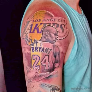 Фото татуировки с портретом Коби Брайанта и логотипом Los Angeles Lakers на плече. Рисунок выполнен в реалистичном стиле с использованием темных и ярких оттенков.