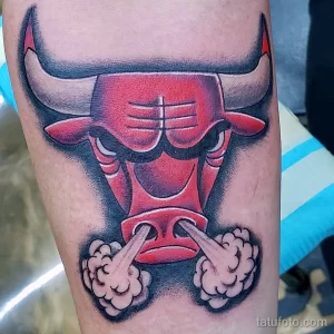 Фото тату на руке с изображением головы быка, символа Chicago Bulls, выполненное в ярких красных и черных тонах с эффектом дыма.